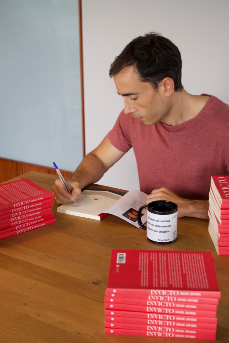 Marcos Vázquez firma un ejemplar de Invicto rodeado de pilas de libros en tapa blanda